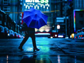 Rear view of woman with umbrella walking in city at night