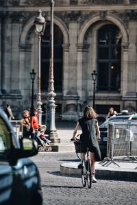 Rear view of woman riding bicycle on street during sunny day