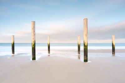 Wooden posts on beach against sky