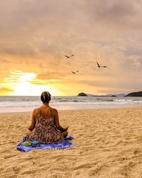 Rear view of woman doing yoga while sitting on beach