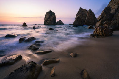 Rocks on beach against sky during sunset