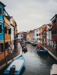 Boats moored in canal amidst buildings in city against sky