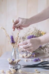 Cropped hands of mature woman arranging flowers in vase on table