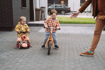 Children playing racing on bike and scooter in the home yard. sister and brother riding fast around