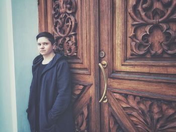 Portrait of beautiful young woman standing against door