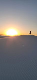 Silhouette person on shore against sky during sunset