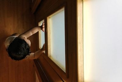 Rear view of man looking through window at home