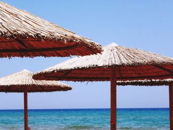 Thatched roofs with calm blue sea against clear sky