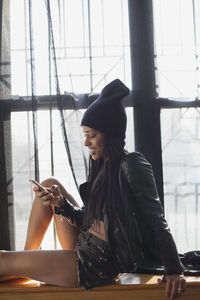 Young woman looking at camera while sitting on window
