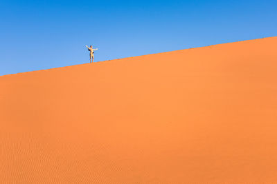 Low angle view of man with arms outstretched standing on sand dune