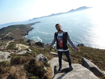 Full length of man standing on rock by sea against sky