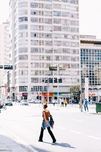 Woman walking on street against buildings in city during sunny day