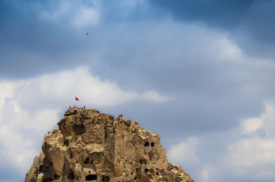 Low angle distant view of people on cliff against cloudy sky