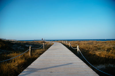 Boardwalk on grass against clear blue sky