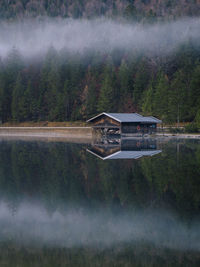 View of hut by lake against misty forest