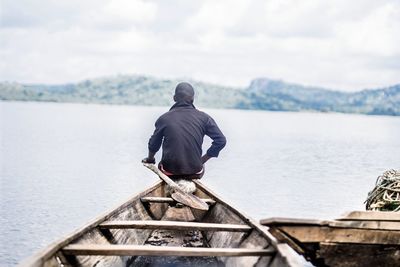 Rear view of man sitting on boat in lake against sky