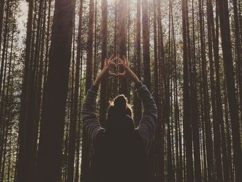 Rear view of woman making heart shape against trees in forest