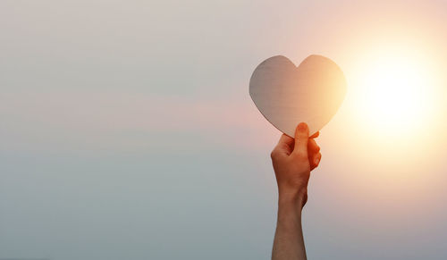 Cropped hand of woman holding heart shape against sky