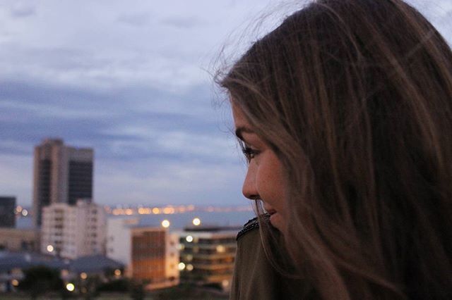 headshot, focus on foreground, lifestyles, person, young adult, sky, leisure activity, head and shoulders, close-up, contemplation, side view, long hair, young women, looking away, brown hair, building exterior, human face, outdoors