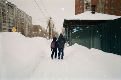 Rear view of people walking on snow covered city during winter
