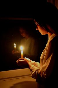 Girl holding lit candle in darkroom