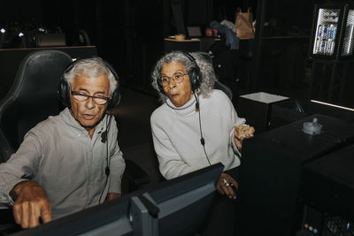 Senior woman looking at computer while male friend playing video game in gaming center