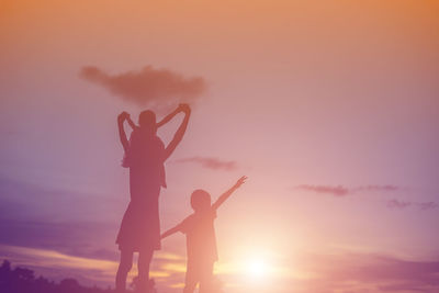 Silhouette people with arms raised against sky during sunset