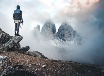 Rear view of man standing on mountain against sky during winter