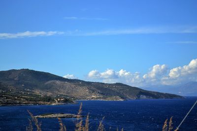 Scenic view of sea by mountains against blue sky