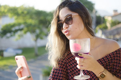 Young woman drinking water from mobile phone outdoors