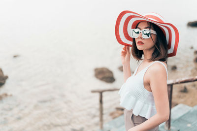 Side view of young woman wearing sunglasses standing against sea