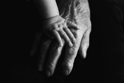 Cropped hand of baby holding hands with grandparent against black background