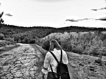 Rear view of woman walking on field against sky