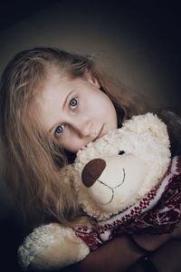 Portrait of girl holding teddy bear against wall