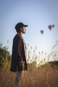Man looking away while standing on field with air balloons in the sky