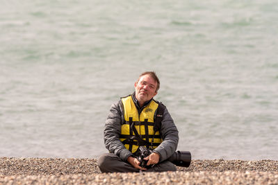 Portrait of man with camera sitting at sea shore