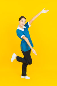 Full length portrait of smiling woman standing against yellow background