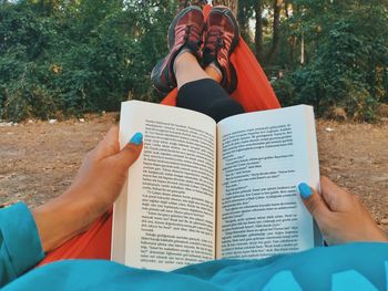 Low section of woman reading book while relaxing on hammock