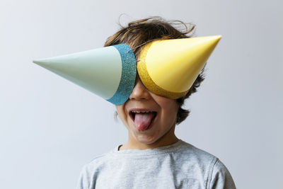 Portrait of little boy with two party hats on his eyes sticking out tongue