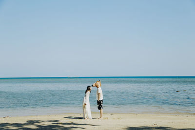 Full length of friends standing at beach against clear sky