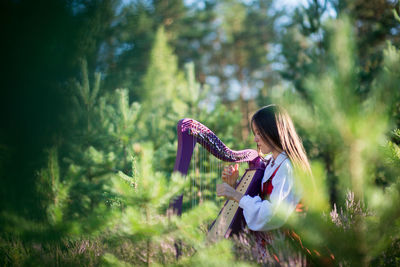 Woman playing harp against trees in forest