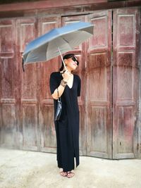Full length of woman holding umbrella while standing against wall