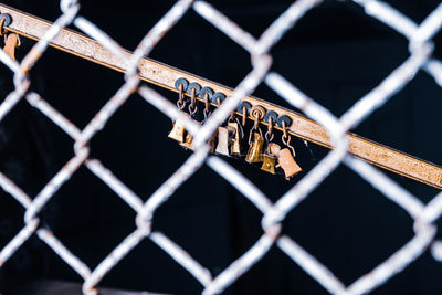 Rusty locks hanging on railing seen through chainlink fence against black background