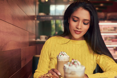 Smiling young woman holding drink in glass at cafe