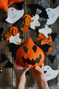 Top view of the boy's hands holding a pumpkin with a face on the background of halloween decorations
