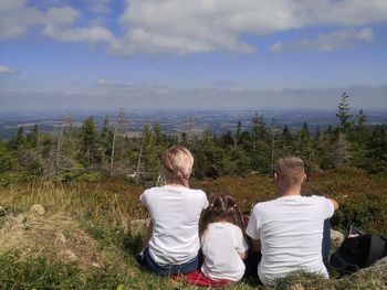 Rear view of people sitting on grass against sky