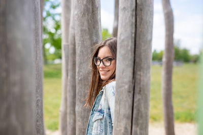 Portrait of smiling young woman standing against tree trunk