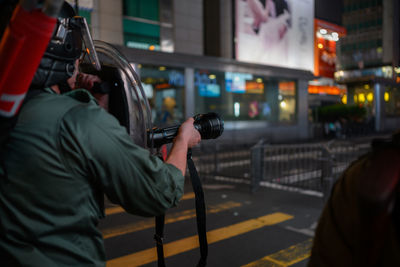 Rear view of man photographing illuminated city street at night