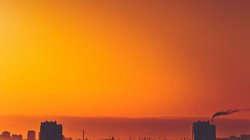 Silhouette buildings against orange sky during sunset