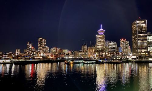 Illuminated buildings by river against sky at night